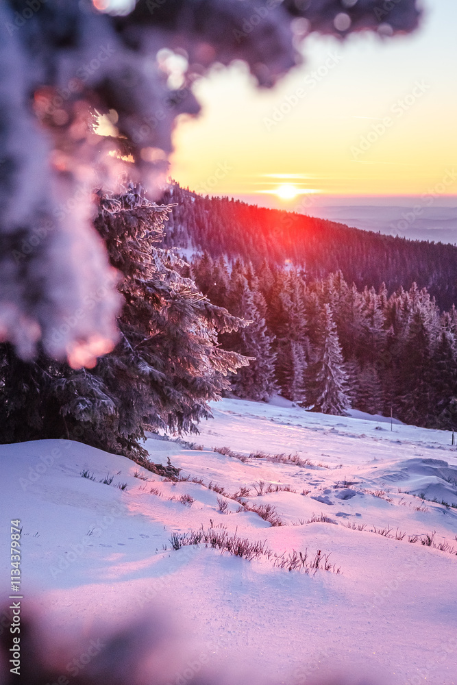 Eastern Sudetes winter landscape, view of sunset and mountain range from mountain hiking trail during winter hike, snow-covered mountainside and illuminated by red sun rays.