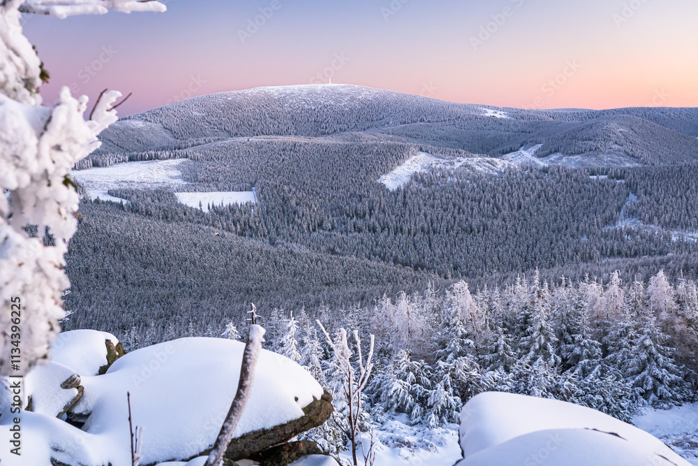 Eastern Sudetes, View of snowy mountain range from hiking trail during winter hike in the mountains, viewpoint of wide winter landscape in the mountains at sunset.