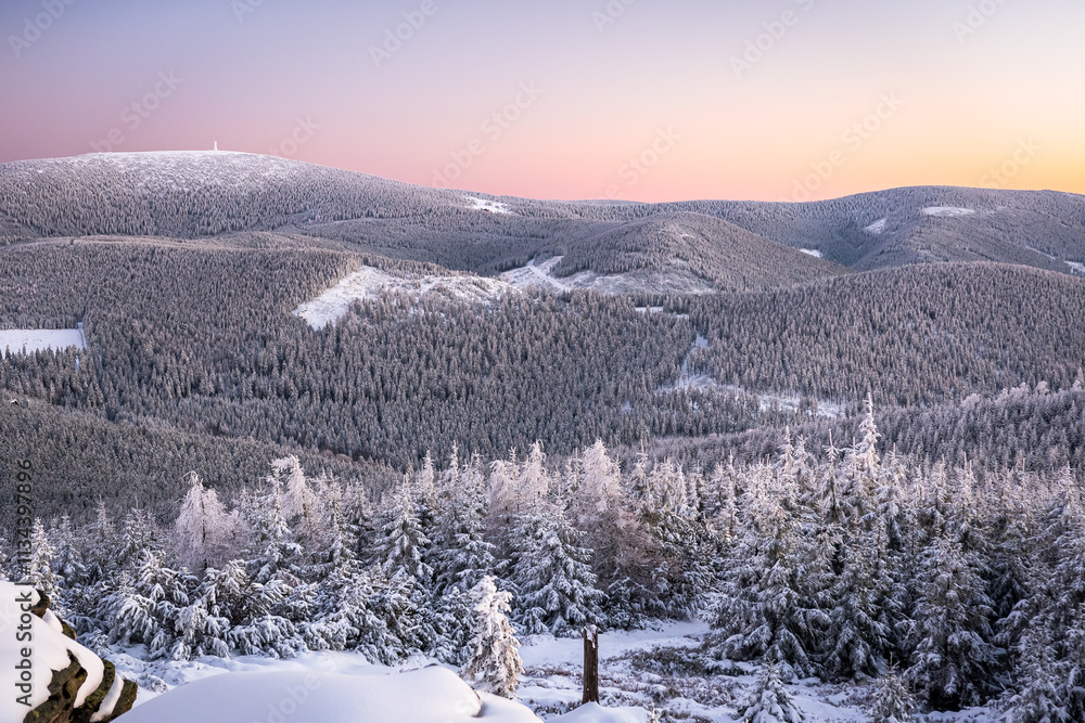 Eastern Sudetes, View of snowy mountain range from hiking trail during winter hike in the mountains, viewpoint of wide winter landscape in the mountains at sunset.