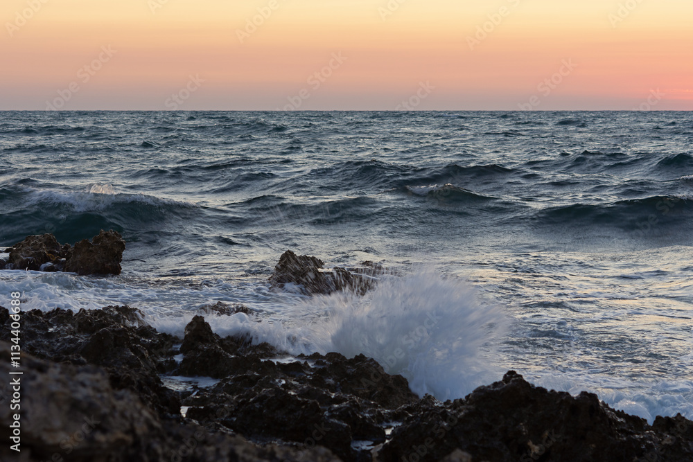 Sunset and storm at sea. Big waves against the setting sun. A summer storm in the ocean. Beautiful sea spray with foam breaks on the rocky shore. Beautiful natural background. The orange setting sun. Sunset and storm at sea. Big waves against the setting sun. A summer storm in the ocean. Beautiful sea spray with foam breaks on the rocky shore. Beautiful natural background. The orange setting sun.