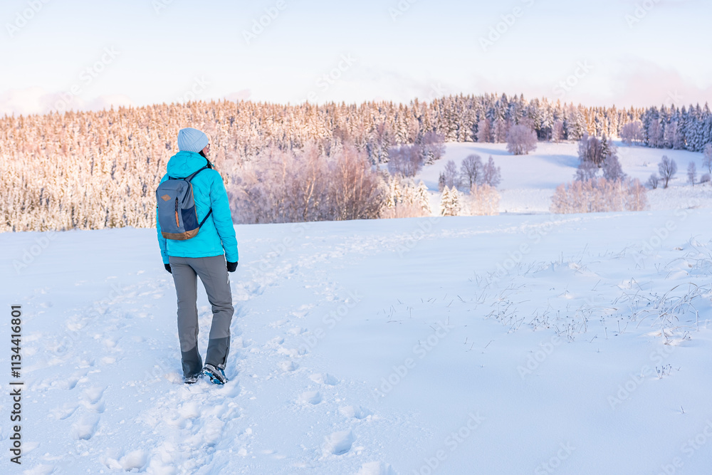 Eastern Sudetes, Young woman on a mountain snow-covered trail, hiking in the white snow and viewing snow-covered hills, winter landscape in the mountains.