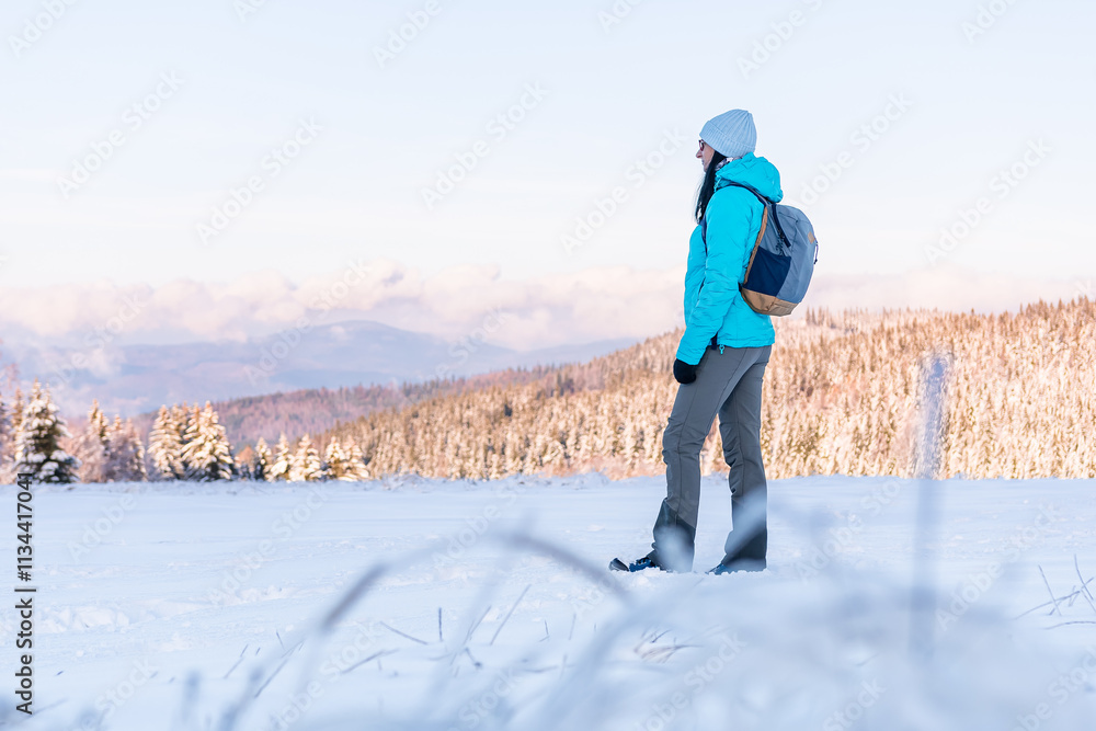 Eastern Sudetes, Young woman on a mountain snow-covered trail, hiking in the white snow and viewing snow-covered hills, winter landscape in the mountains.