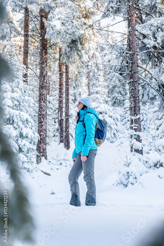 Obraz na płótnie Eastern Sudetes, Young woman hikes on a mountain snow-covered trail, walks on white snow through the forest and looks at the snow-covered trees, winter landscape in the mountains. w salonie