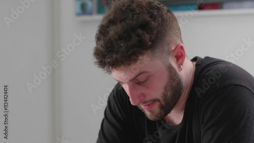 A young man with dark hair and beard, sitting at a university desk, looking desperate and disappointed over a failed exam, capturing a moment of academic stress.