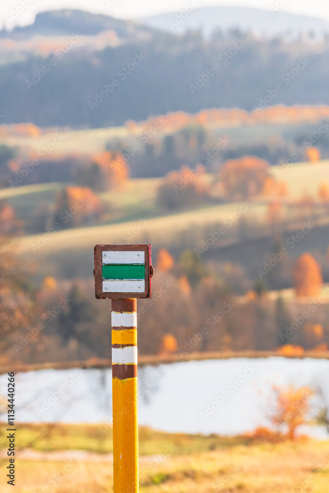 Czech Republic, Stribrnice, yellow and green hiking trail markings on a post. Autumn panorama of hills and fields, view from the hiking trail in the late evening.
