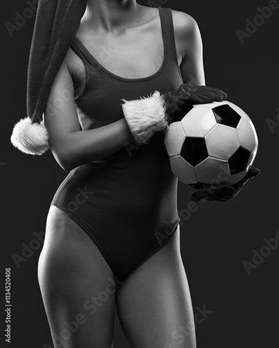 Beautiful sexy girl in red bodysuit in red santa hat holding black and white soccer ball on red background. photo