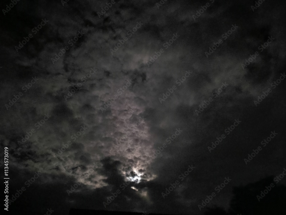 This image shows a partly cloudy night sky with moonlight filtering through the gaps in the clouds.