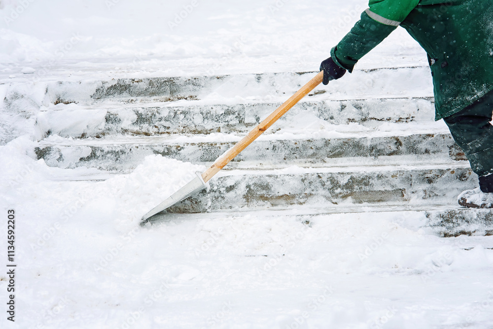 Worker removing snow from slippery stair steps with snow shovel in city during snowstorm, winter cleanup efforts and safety precautions