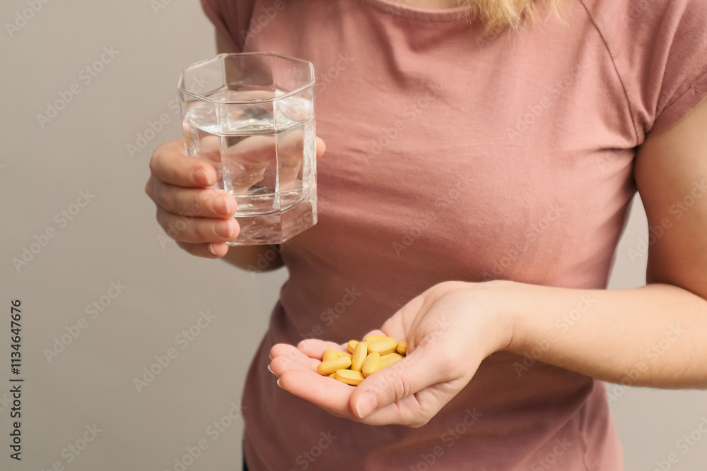 Woman's hands with pills and glass of water. Woman holding yellow pill on hand and drinking water in glass Woman's hands with pills and glass of water. Woman holding yellow pill on hand and drinking water in glass
