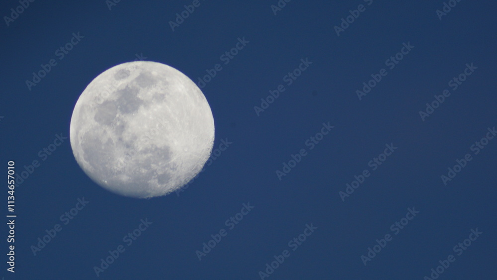A bright full moon shining in a dark blue night sky surrounded by soft clouds and lunar craters visible A bright full moon shining in a dark blue night sky surrounded by soft clouds and lunar craters visible