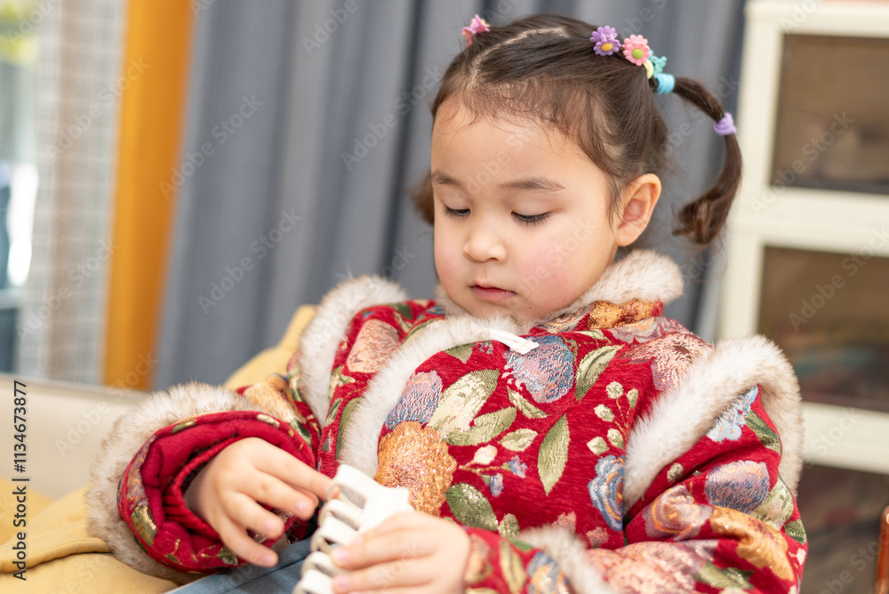 Small Chinese, multiracial girl is ready for a celebration of Chinese New Year. She is posing for a photo in her traditional Chinese dress Small Chinese, multiracial girl is ready for a celebration of Chinese New Year. She is posing for a photo in her traditional Chinese dress