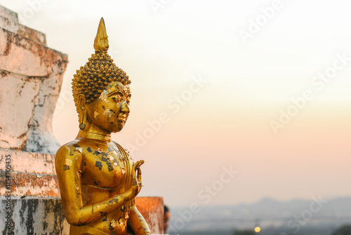 Golden Buddha statue is positioned in a seated posture with gold leaf on surface at sunset photo