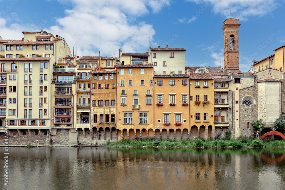 Colorful medieval houses sit above the Arno River in Florence, showcasing vibrant facades and historical architecture under blue cloudy sky. Colorful medieval houses sit above the Arno River in Florence, showcasing vibrant facades and historical architecture under blue cloudy sky.