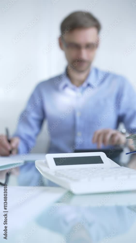 Calculator and accounting papers are on the glass desk. Man accountant using calculator on the background. Audit and taxes in business Calculator and accounting papers are on the glass desk. Man accountant using calculator on the background. Audit and taxes in business