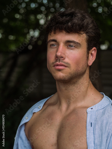 Male model with short curly hair poses outdoors in relaxed setting