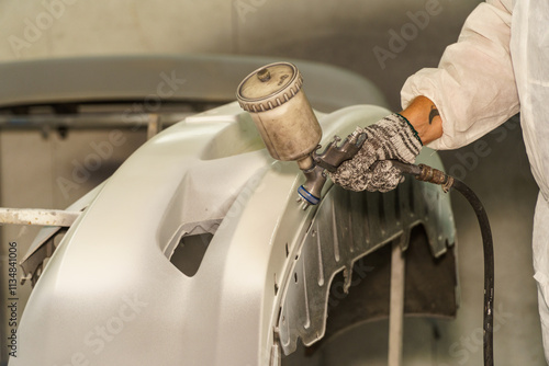 Professional worker applying paint to a vehicle part using a spray gun in a workshop setting during daylight hours