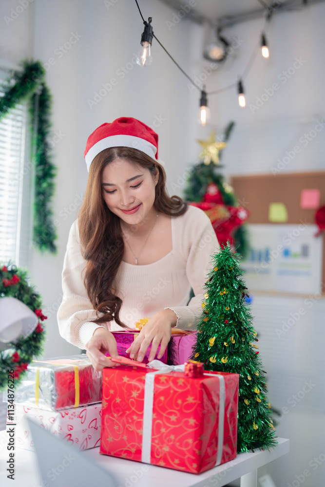 Young asian woman wearing santa hat wrapping christmas gifts at her home office desk, surrounded by christmas decorations and string lights Young asian woman wearing santa hat wrapping christmas gifts at her home office desk, surrounded by christmas decorations and string lights