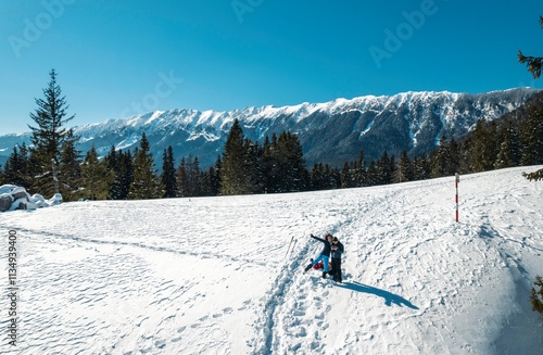 Captivating snowy terrain amidst the breathtaking Piatra Craiului Mountains, where adventurers engage in playful activities under a clear blue sky, surrounded by evergreen trees photo