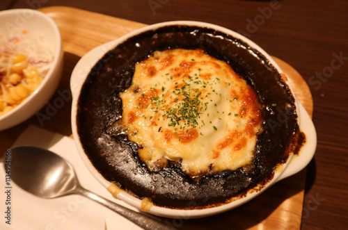 close up of baked Japanese curry with cheese on top on a plate with salad on the side on a wooden tray