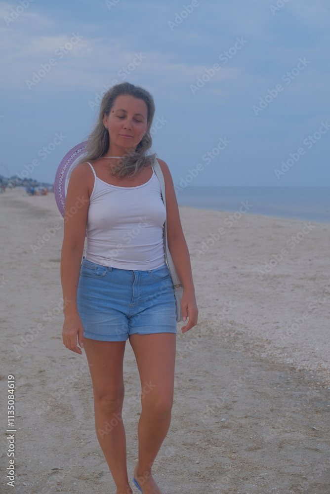 person on the beach woman walking on the seashore with a hat in summer autumn spring looks at the area water sky European appearance there are emotions on her face in shorts and a T-shirt beautiful ap person on the beach woman walking on the seashore with a hat in summer autumn spring looks at the area water sky European appearance there are emotions on her face in shorts and a T-shirt beautiful ap
