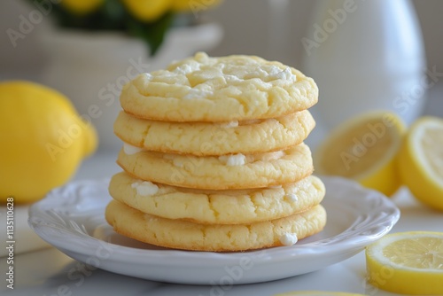 Lemon cookies stacked on a plate with fresh lemons and flowers in background