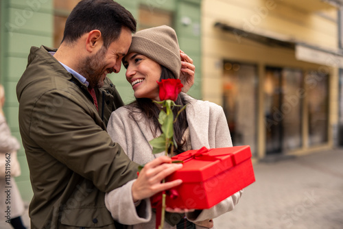 Billede på lærred A joyful Caucasian couple embraces, exchanging a red rose and gift box on Valentine's Day