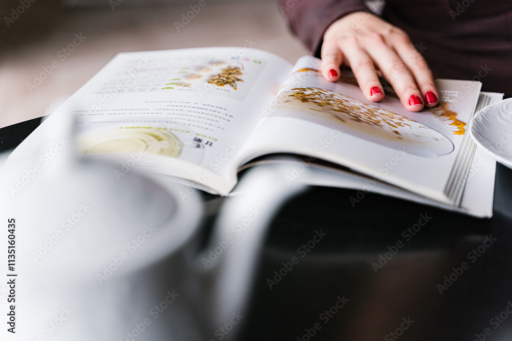 Female hand gently rests on an open book on a table.