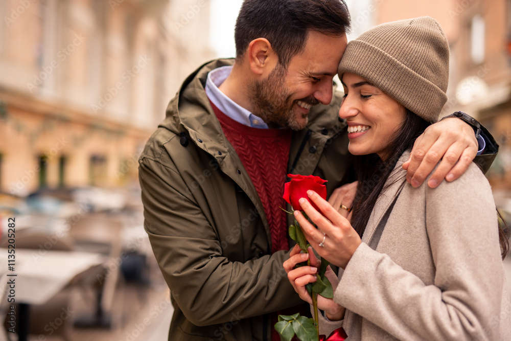 A mid adult Caucasian man surprises his partner with a rose in a cityscape setting. They are dressed in casual winter attire, creating a warm, intimate moment. A mid adult Caucasian man surprises his partner with a rose in a cityscape setting. They are dressed in casual winter attire, creating a warm, intimate moment.