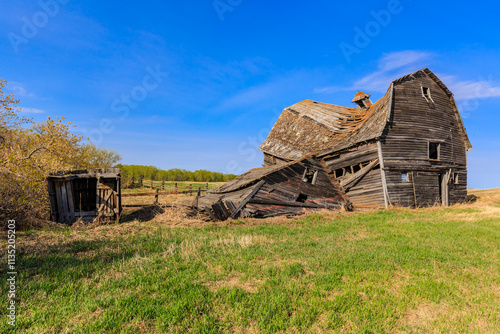 Obraz na plátně A dilapidated old farmhouse sits in a field with a blue sky overhead