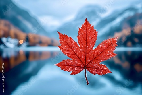 Red maple leaf in focus image against autumn mountains with snow covered peaks and dense forest in autumn colours. Place in Canada. Location for copying