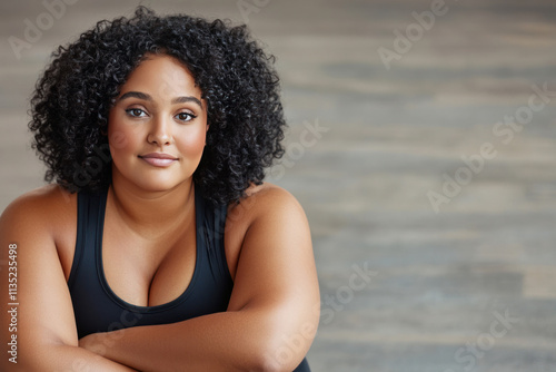 Confident young woman with curly hair poses in a casual black tank top against a neutral background