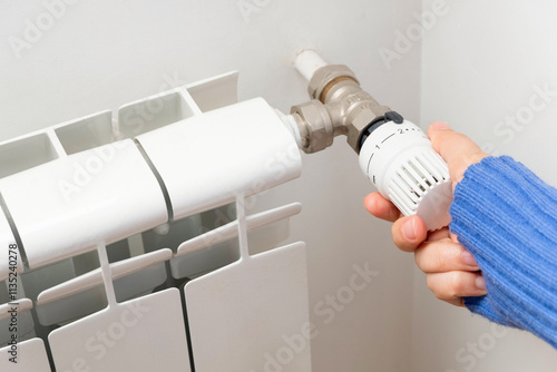 Hands adjusting modern radiator thermostat at home