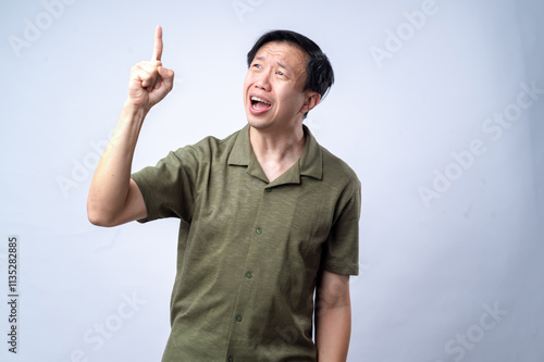 An Asian man in a casual green shirt excitedly points upward with one finger, mouth open in expression, standing against a clean white background. The image conveys an idea, realization photo