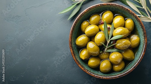 Green olives arranged in a bowl with fresh olive leaves on a dark surface