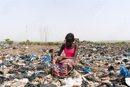 Φωτογραφία Young African girl searching for food and reusable items in a garbage dump, a sy