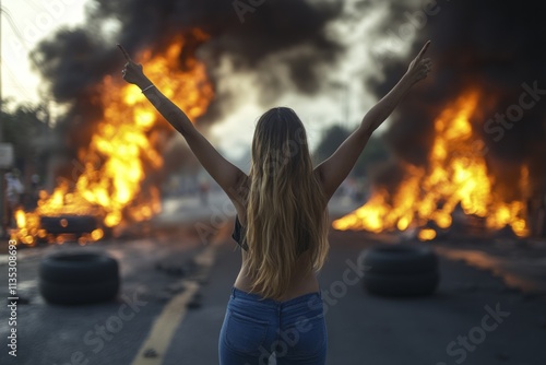 Young woman protesting raising arms in front of burning barricade in street photo