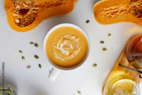 Roasted butternut squash soup with cream and pumpkin seeds on two white mugs. photo