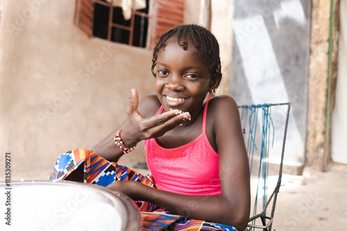 Cute little African girl licking her fingers after a delicious rice porridge photo