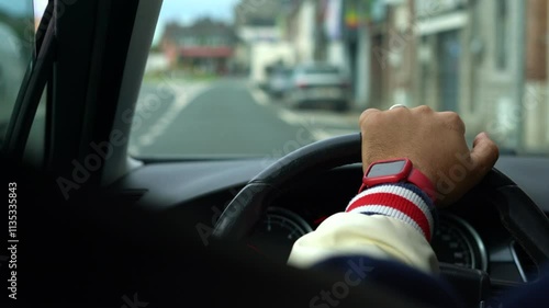 A closeup of a hand gripping a steering wheel while driving in the city