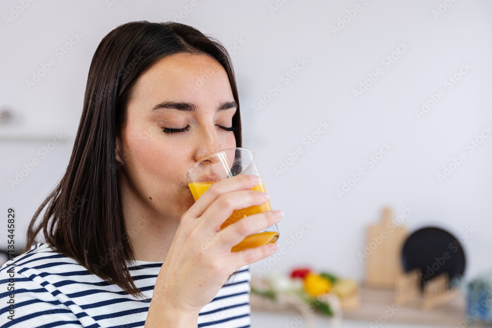 Vertical shot of young beautiful woman drinking natural orange juice in the morning in the kitchen at home. Healthy lifestyle concept Vertical shot of young beautiful woman drinking natural orange juice in the morning in the kitchen at home. Healthy lifestyle concept