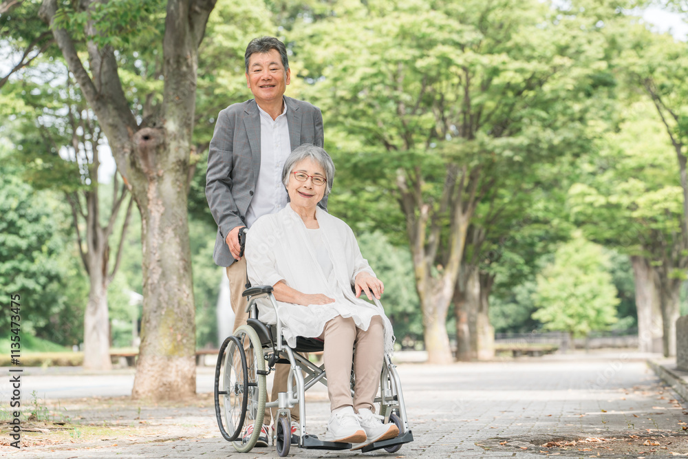 車椅子で公園を散歩するシニア・高齢者夫婦（介護）
