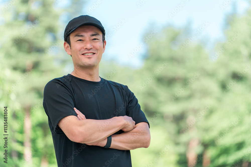 Fototapeta premium 新緑の公園でスポーツウェアを着て腕組みをするアジア人男性 