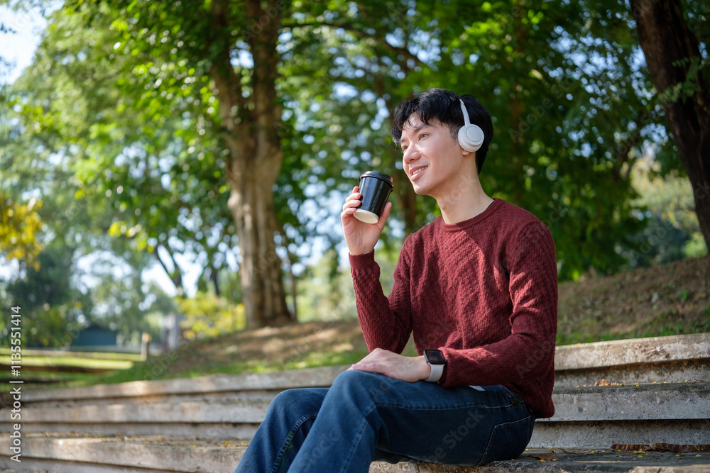 Relaxed and carefree, young man  enjoying a warm beverage and listening to music in a serene park.