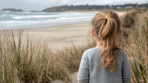 Child observes the shoreline while standing amidst grass by the beach