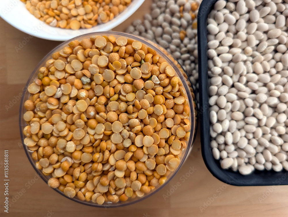 White beans in a black container and small, yellow, split peas in a clear container and white bowl White beans in a black container and small, yellow, split peas in a clear container and white bowl