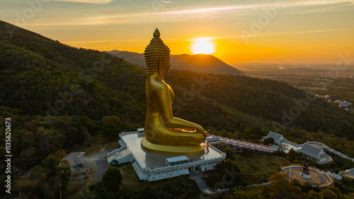 An awe-inspiring view of a big golden Buddha statue atop a hill overlooking a serene valley, captured during the vibrant colors of sunset. aerial view of The biggest golden Buddha at Lopburi Thailand