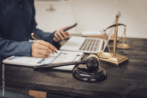 Close-up of an Asian female lawyer sitting at her desk in a law office. A wooden hammer and brass scales symbolize justice. She demonstrates expertise in the legal and justice process photo