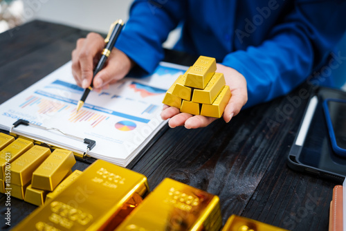 Bild auf Leinwand An Asian businesswoman sits at her desk analyzing gold bar prices, buying and selling gold, trading gold stocks, monitoring charts, and studying currency trends in an uptrending stock market