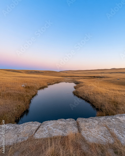 Serene landscape at dusk with a calm stream running through golden grasslands