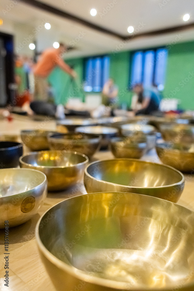 Close-up view of Tibetan singing bowls in a wellness studio with blurred background showing people engaging in a sound healing session or meditation activity Close-up view of Tibetan singing bowls in a wellness studio with blurred background showing people engaging in a sound healing session or meditation activity